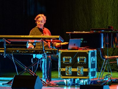 A man under orange and blue lighting playing two keyboards at the same time