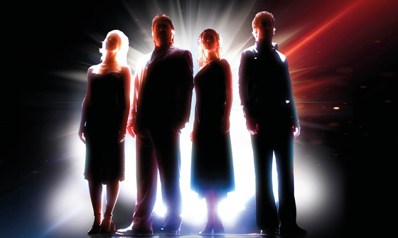 The silhouettes of two men and two women can be seen, from behind they're lit by white, red and blue light