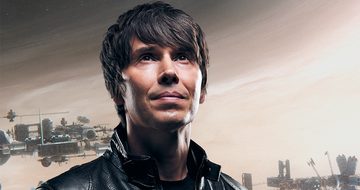 Brian Cox wearing a leather jacket and looking up towards the sky. The sky behind him is beige with sci-fi looking spaceships behind him