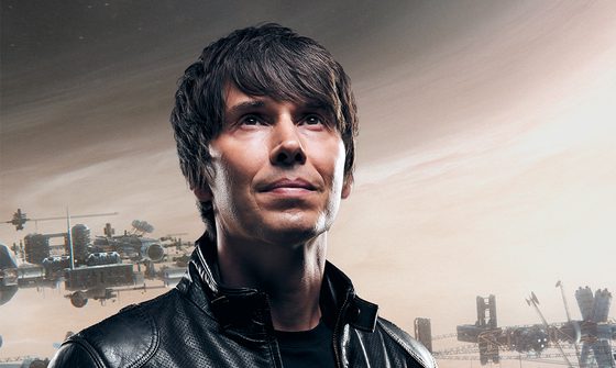 Brian Cox wearing a leather jacket and looking up towards the sky. The sky behind him is beige with sci-fi looking spaceships behind him