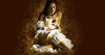 A woman in a white dress in sat in straw holding a rose looking at the camera