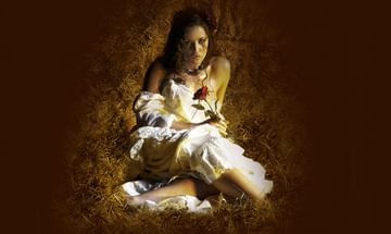 A woman in a white dress in sat in straw holding a rose looking at the camera