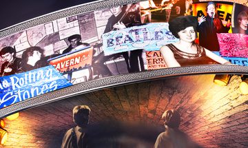 A collage of different artists and their posters that have been to The Cavern Club over the years including The Rolling Stones, The Beatles, Cilla Black, and Adele, on an arch above the brick ceiling of the club with two men looking up at it