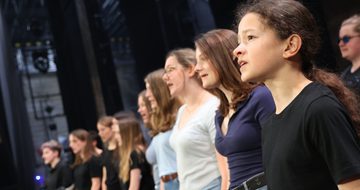 A group of young people in casual clothing stand in rows as they sing together