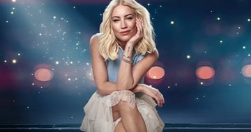 Denise Van Outen, a woman with blonde hair sitting gracefully against a sparkling, starry background wearing a light blue top and a white lace skirt