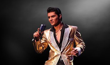 Emilio in a black shirt and gold blazer, with his black hair quaffed like Elvis' holding a microphone