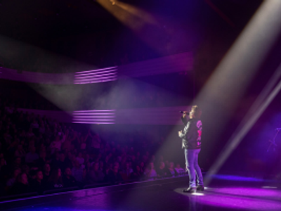 Lit by a spotlight a man in a leather jacket sings out to a large crowd