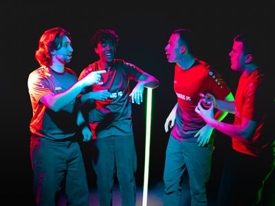 Lit by pink and blue light four men in red football shirts stand around chatting like they're at a bar