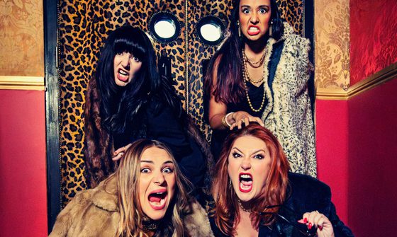 Four women in fur coats pretend to roar at the camera while stood in front of leopard print doors