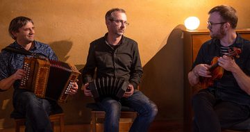 Three men all holding instruments in a softly lit room looking at each other