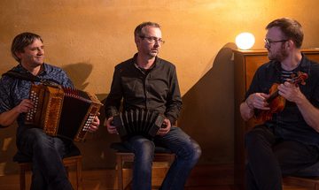Three men all holding instruments in a softly lit room looking at each other