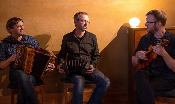Three men all holding instruments in a softly lit room looking at each other