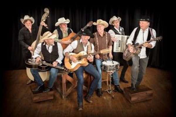 Seven men in shirts, waistcoats and cowboy hats all sat together holding various instruments