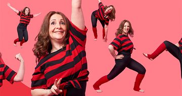 Lucy Porter, a cheerful woman in a red and black striped shirt striking playful poses against a pink backdrop