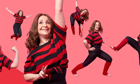 Lucy Porter, a cheerful woman in a red and black striped shirt striking playful poses against a pink backdrop