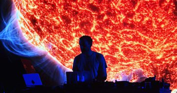 Max Cooper is a silhouette as he DJs in front of a huge projection of a sun