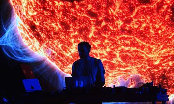 Max Cooper is a silhouette as he DJs in front of a huge projection of a sun
