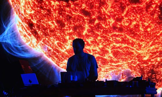 Max Cooper is a silhouette as he DJs in front of a huge projection of a sun
