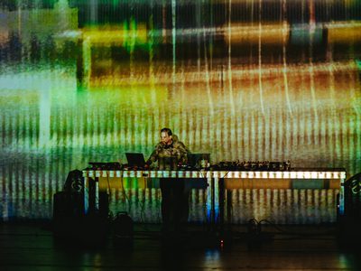 An abstract green and yellow striped design is projected on and behind Max Cooper