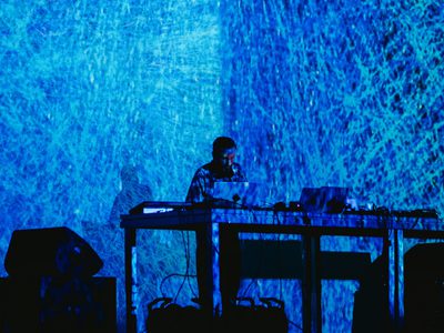 An abstract blue background, almost like ice is projected over and behind Max Cooper as he performs