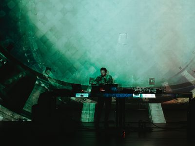 An abstract green and white design, almost like tiles is projected over and behind Max Cooper