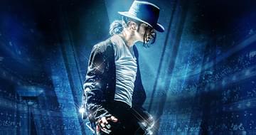 A side profile of Ben Bowman as Michael Jackson. He is wearing a dark fedora, a white shirt and black jacket, and he is performing under dramatic blue stage lights