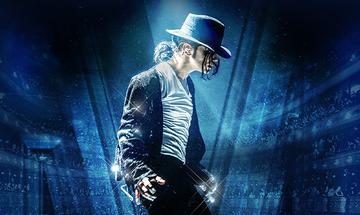 A side profile of Ben Bowman as Michael Jackson. He is wearing a dark fedora, a white shirt and black jacket, and he is performing under dramatic blue stage lights