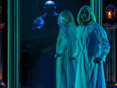 A woman in a white gown looking startled beside a large, ornate mirror with a mysterious, dark figure behind the glass, in a dark room