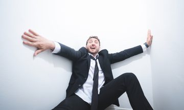 Wearing a suit and tie, Seann Walsh, a young comedian with messy brown hair, pushes at the big white walls which look to be closing in on him