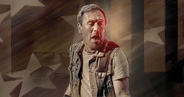 A Bruce Springsteen impersonator in a t-shirt and vest with his mouth open playing a guitar which is just out of shot