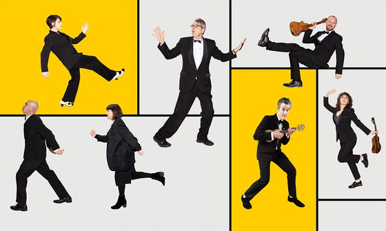 Seven members of The Ukulele Orchestra in tuxedos, and black outfits all in a different silly position, three are holding ukuleles. They're on a background of different sized grey rectangles with two yellow ones