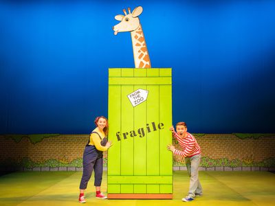 A man and woman next to a large green crate with a giraffe head sticking out the top