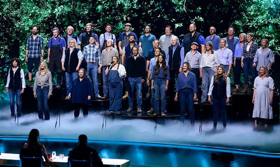 A large group of farmers all dressed in blue stood on the Britain's Got Talent stage with fog around their feet and foliage projected behind them
