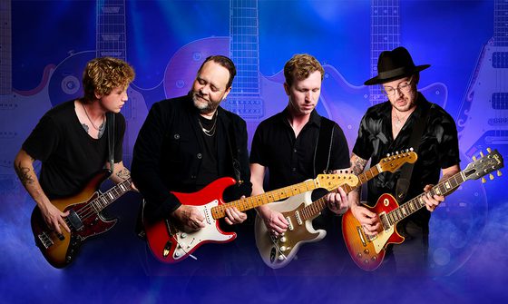 Four musicians performing with guitars, set against a backdrop of large guitars on a purple haze background
