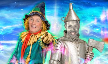 Bobby Davro dressed as a scarecrow and Stevi Ritchie dressed as the Tin Man standing together smiling. Bobby is pointing at the camera and Stevi is holding an axe