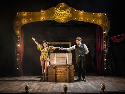 Two actors performing on stage in Houdini's Greatest Escape; a man and a woman are stood either side of a wooden box