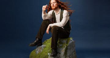 Alasdair Beckett-King sat on a rock pointing and looking out into the distance