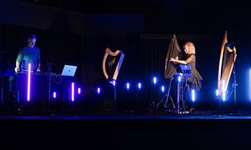 Ruth Wall and Graham Fitkin performing on stage with various harps, surrounded by blue lighting
