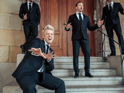 G4 standing on stone steps with Jonathan Ansell pointing his hands towards the camera and his mouth open