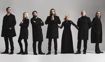 Rumours of Fleetwood Mac stood in a line wearing all-black outfits on a grey background