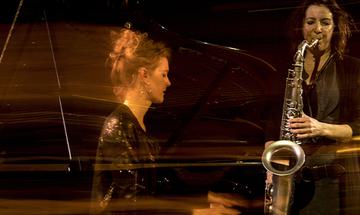 Tori Freestone playing a saxophone and Alcyona Mick playing a piano
