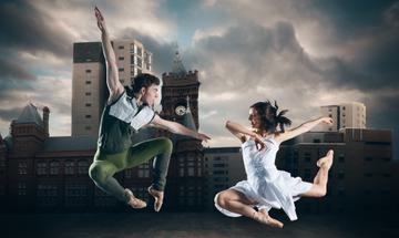 Two dancers mid-air with a city landscape behind them