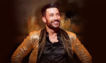 Giovanni Pernice with his hands on his hips, smiling and looking up away from the camera. He is wearing a black shirt and gold sparkly jacket
