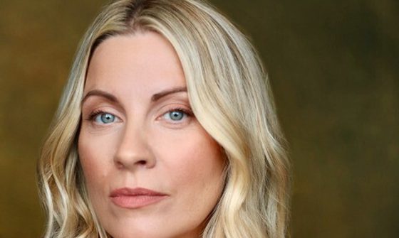 Louise Dearman a white, blonde woman in a red blouse with a neutral expression