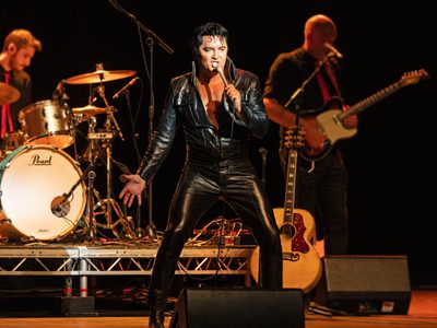 Ben Portsmouth as Elvis wears a tight black leather jumpsuit and he sings passionately into a microphone