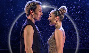 Carlos wears his hair slicked back and a black sleeveless vest. Amy faces him wearing a sparkly dress and her hair in a high bun.