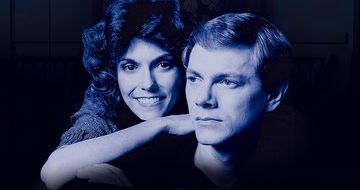 A blue photo of the Carpenter siblings when they were young. Karen in leaning on Richard's shoulder smiling while he looks off into the distance