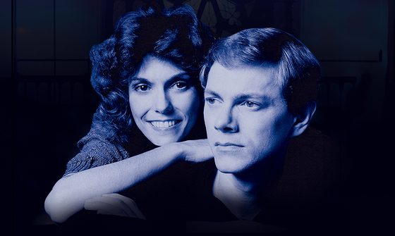 A blue photo of the Carpenter siblings when they were young. Karen in leaning on Richard's shoulder smiling while he looks off into the distance