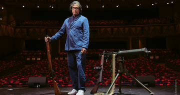 David Olusoga stood on stage with a rifle in one hand and more weapons to his left on stage