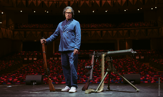 David Olusoga stood on stage with a rifle in one hand and more weapons to his left on stage